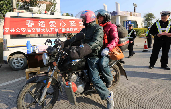 A couple on a motorcycle takes a break to enjoy free refreshments at a temporary station in Liuzhou, Guangxi Zhuang autonomous region, on Tuesday. Police set up temporary stations during the Spring Festival travel rush to assist migrant workers heading home. Deng Liting / Xinhua
