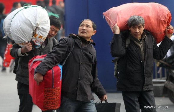 Passengers carrying bags walk outside the Shanghai Railway Station, east China's Shanghai, Jan. 18, 2014. A long-distance-journey on train can't discourage people's longing for reunion with family members during the Chinese Lunar New Year. They tried all means to get a ticket heading back for hometown ahead of the festival. (Xinhua/Pei Xin)  