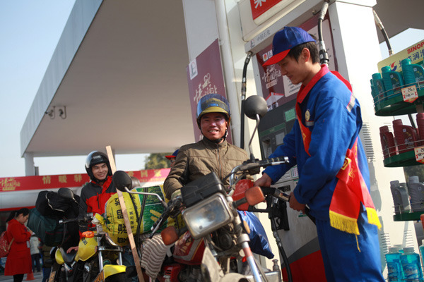 A worker of Sinopec Guangdong Oil Products Company offers free gas to migrant workers who are traveling home by motorbike in Foshan, Guangdong province, Jan 23, 2014. Qiu Quanlin / China Daily