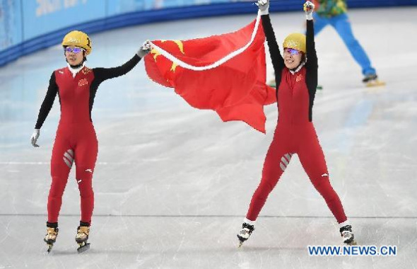 Winner China's Zhou Yang (R) holds up her national flag along with compatriot Li Jianrou after the women's 1,500 metres short track speed skating finals race at the Iceberg Skating Palace at the Sochi 2014 Winter Olympic Games February 15, 2014. [Photo: Xinhua]