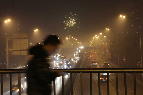 A pedestrian walks across an overpass on Beijings South Third Ring Road as fireworks light up the smoggy sky on Friday, Lantern Festival. WANG YUELING / FOR CHINA DAILY 