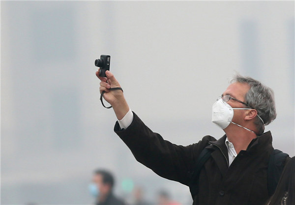 The smog-stricken Beijing will see mild rainfall on Wednesday afternoon, then gales at night, expected to disperse the week-long notorious smog, China's Central Meteorological Observatory forecast on Wednesday morning. A visitor wearing a mast takes a picture at the Tian'anmen Square on a dazy day on Feb 25, 2014. 