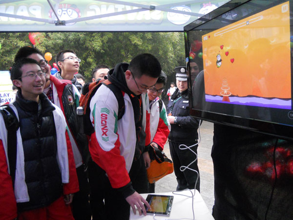 A high school student (center) plays the Saving Pandas game during his visit to the Chengdu Research Base of Giant Panda Breeding in Sichuan province on Friday while his classmates watch a television screen showing his moves. Photo by Huang Zhiling