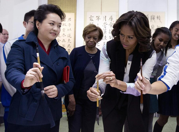 Peng Liyuan (L), wife of Chinese President Xi Jinping, shows US first lady Michelle Obama how to hold the writing brush as they visit a Chinese traditional calligraphy class at the Beijing Normal School, a school which prepares students for university abroad, in Beijing March 21, 2014. [Photo/Agencies]