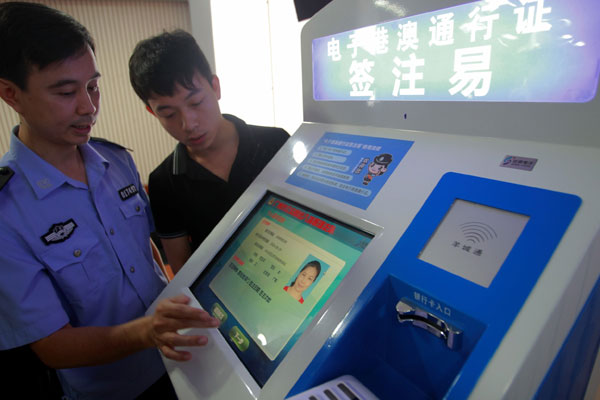 An official from the Guangzhou exit-and-entry police shows how to use a self-service machine for the new e-permit, created for people commuting between the mainland and Hong Kong and Macao. Zou Zhongpin / China Daily
