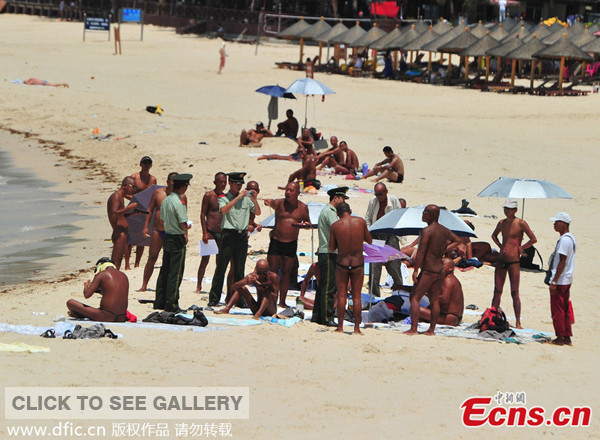 Police officers hand out printed notices and persuade tourists not to skinny dip and sunbath naked at Dadonghai Beach in Sanya of south China's Hainan province on May 4, 2014. [Photo/IC]