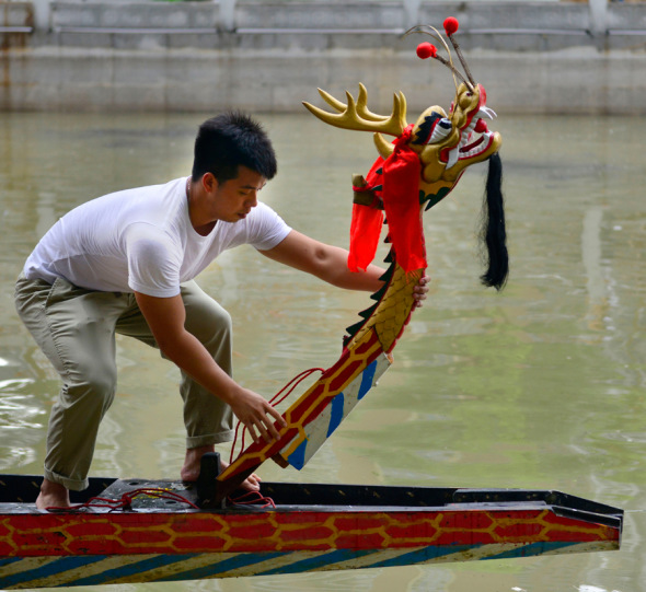 A villager installs the head of a dragon boat in preparation for its maiden trip in Guangzhou, Guangdong province. Villagers hope the boat will bring luck to the village. Gao Dianhua / for China Daily