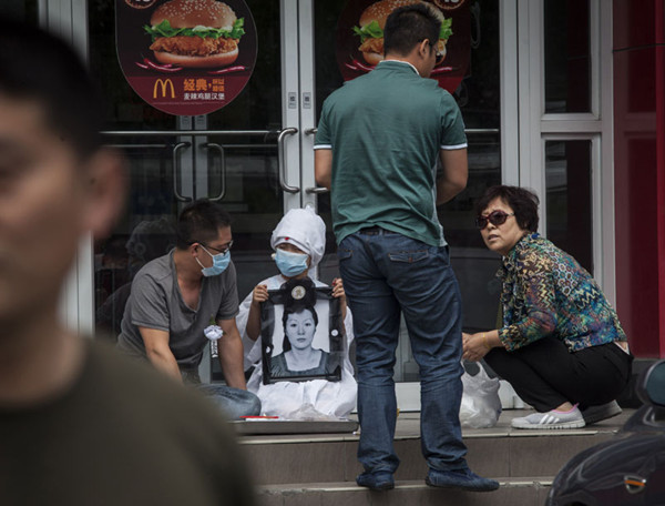 The husband (left, with mask) and son (second to left) of a murder victim, together with other relatives, mourn the death of Wu Shuoyan in front of a McDonald's restaurant in Zhaoyuan, Shandong province, on Tuesday. Wu was severely beaten inside the restaurant on May 28, allegedly by six cult members, and died in a hospital. Kou Cong / For China Daily