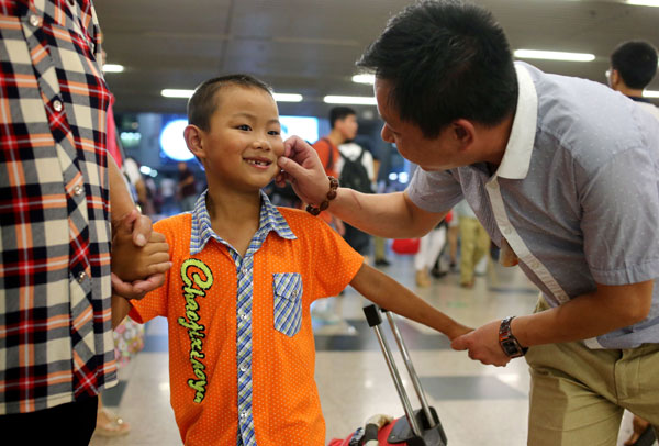 Li Lianjun checks the new smile of his son Li Hao, who arrived at the Beijing West Railway Station from his hometown in Jiangxi province. Children of migrant workers oft en visit their parents in big cities as the summer holidays begin.[Wang Jing/China Daily]
