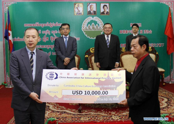 Zhou Xinzheng (1st L), visiting deputy secretary general of the China Association for International Friendly Contact, hands over 10,000 US dollars to Ly Kong Iv (1st R), president of the Cambodia-China Culture & Economy Association (CCCEA), in Phnom Penh, Cambodia, July 10, 2014.  (Xinhua/Sovannara) 