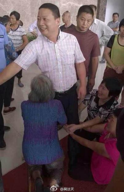 The official smiling and shaking hands with other people in front of three kneeling women, one of them over 80 years old and sobbing. (Photo: screenshot from Weibo)