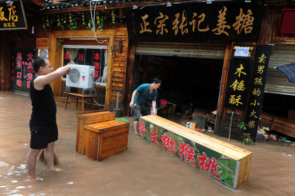 Shop owners clean up the mess after floodwaters receded in the ancient-town resort of Fenghuang in Hunan province on Wednesday. Heavy downpours hit a large part of southwestern China, killing at least 32 and displacing tens of thousands. Guo Liliang / for China Daily