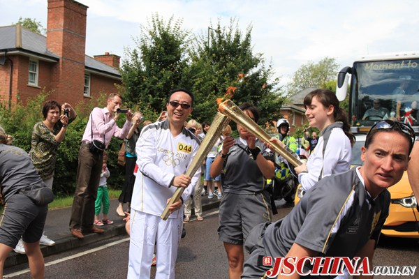 Wang Jian passes the Olympic flame to a British torch bearer during the London Olympic torch relay in 2012. [File photo provided for jschina.com.cn]
