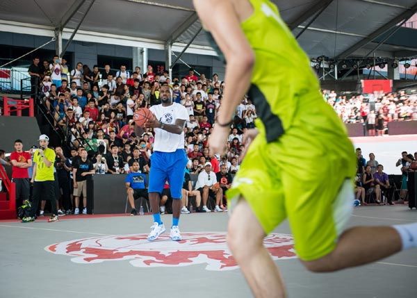James (left) passes a ball to a young player during an exhibition game on the outdoor court of Hi-Park in Beijing on Monday. [Photo provided to China Daily]