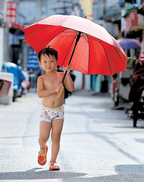 A little boy in just his undergarment walks in the shade of a huge umbrella in downtown Shanghai yesterday. With the unrelenting summer heat, local hospitals are forced to deal with a jump in patients. But Typhoon Matmo is expected to bring down the mercury this week.  Wang Rongjiang/Shanghai Daily