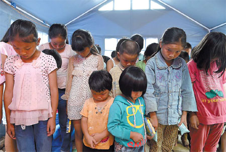 Children at a temporary home in Ludian county, Yunnan province, take part in a memorial service on Sunday for people killed in the magnitude-6.5 earthquake on Aug 3. Zhang Wei / for China Daily