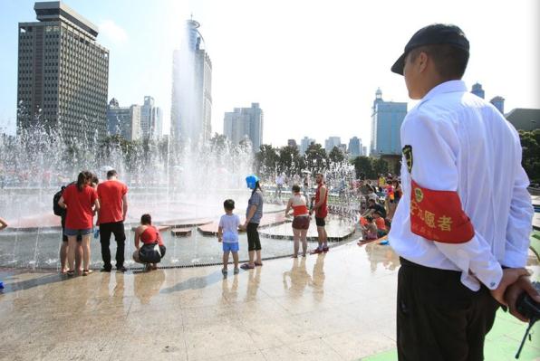 People have fun playing with water at the Peoples Square in Shanghai as a security guard looks on. (Photo: Shanghai Daily)
