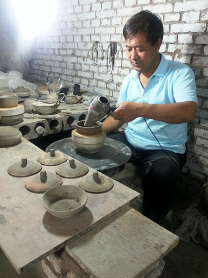 An artist air-dries completed cooking pots in his workshop in Pingding county, Shanxi province, Aug 7. [Photo by Wei Biao/Xinhua News Agency]
