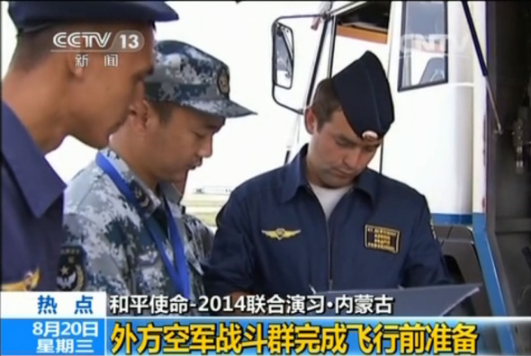 A Chinese supporting staff (center) assists foreign air troops to prepare for the first flight training of Peace Mission-2014. [Photo: screenshot from CNTV.cn]