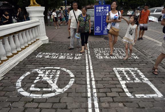 People walk on a sidewalk that is divided into two sections - one for those using cell phones, and the other for those who are not - in Chongqing on Saturday. Ran Wen / for China Daily