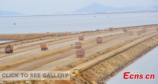 Photo taken on September 14, 2014, shows trucks running on the Jinzhouwan International Airport construction site to remove soil from a mountain nearby to the offshore area. [Photo: China News Service/ Liu Debin]