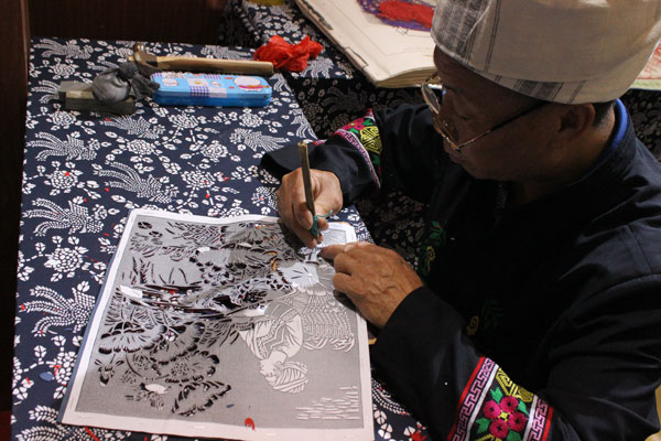 A man of Tu ethnic group performs paper-carving at the third China Intangible Cultural Heritage Exhibition in Jinan, the capital city of East China's Shandong province, Oct 10, 2014. [Photo by Wang Kaihao/China Daily]