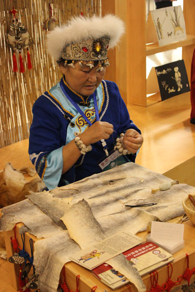 A woman of Hezhe ethnic group from Heilongjiang province shows fish-skin painting skills at the Third China Intangible Cultural Heritage Exhibition in Jinan, East China's Shandong province, Oct 10, 2014. [Photo by Wang Kaihao/China Daily]   