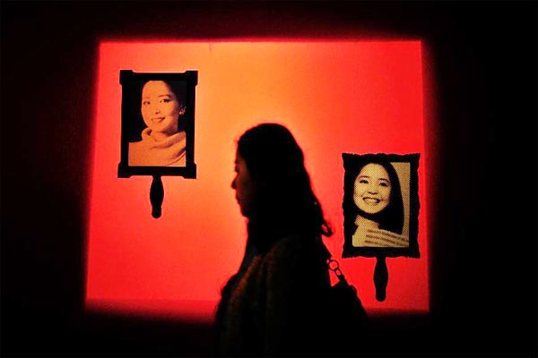 A visitor walks past pictures of singer Teresa Teng during a special exhibition on Teng, at the Hubei provincial museum in Wuhan, capital of Central China's Hubei province, March 28, 2014.[Photo/Xinhua]