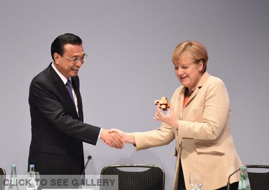 Chinese Premier Li Keqiang (L) presents a burr puzzle to German Chancellor Angela Merkel as they attend a China-Germany economic and technological cooperation forum in Berlin, Germany, Oct. 10, 2014. (Xinhua/Li Xueren)