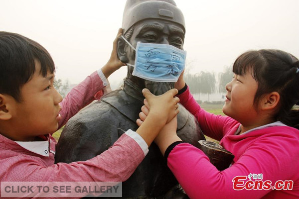Children put mask on a sculpture to 'protect' it from smog during an environmental awareness campaign at their school in Guangping county, North China's Hebei province on Friday, October 10, 2014. [Photo: China News Service/ Cheng Xuehu] 
