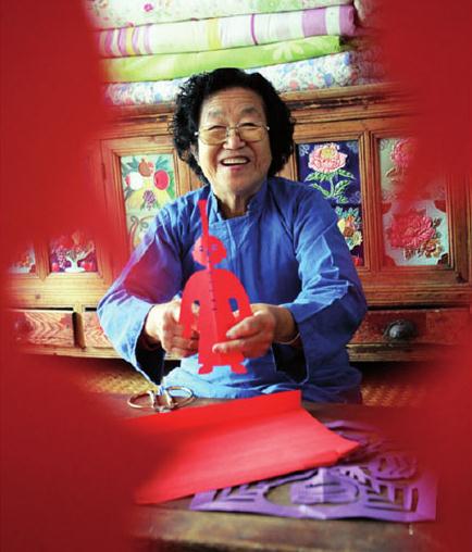 Ni Youzhi, a 76-year-old paper-cutting craftswoman, shows her artwork. [Photo by Zhang Wei/China Daily]