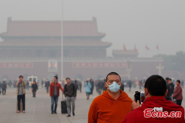 A man wearing mask poses for a photo amid heavy smog at Tian'anmen square in Beijing on Wednesday, November 19, 2014. Beijing's air quality index hit 348 at 4 pm with the index of PM2.5, the smaller but more harmful particles, also reaching the same level, said the website of the Beijing Environmental Protection Monitoring Center. [Photo: China News Service/ Song Hantao] 
