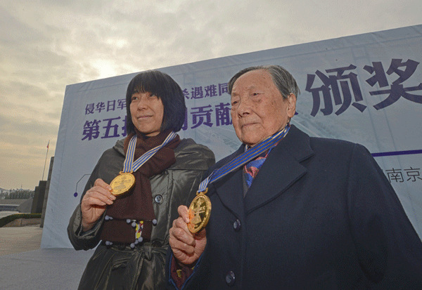 Xia Shuqin (right), a survivor of the Nanjing Massacre, and Yamauchi Sayoko, a Japanese priest, show their medals at a award ceremony in Nanjing, Jiangsu province, on Tuesday. They were awarded for their special contribution to the Memorial Hall of the Victims in the Nanjing Massacre by Japanese Invaders. Cui Xiao / for China Daily  