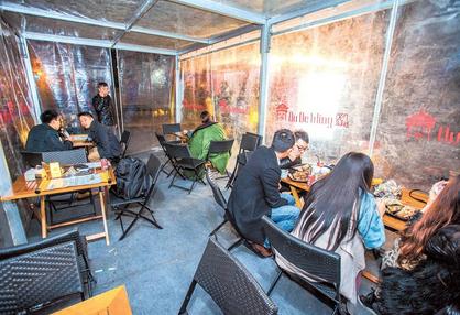 Diners tuck into grilled food in a tented area, while food is prepared in a trailer at the Nu De Wing kebab and grill stalls latest home on Dagu Road on Sunday.  Gao Jianping