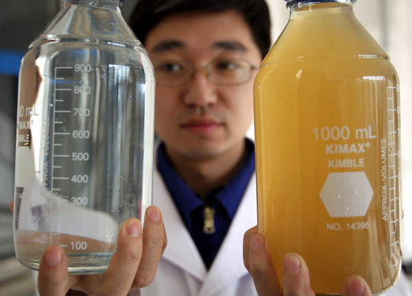 A staff member of the Beijing Waterworks Group shows off a bottle of untreated water and a bottle of water purified by membrane-ultrafiltration technology. [Photo/China Daily] 