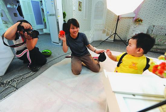 A "laugh producer" waves her arm to induce a smile on a child during a shoot in a photographic studio in Wenzhou, Zhejiang province, June 23, 2014. [Photo/Xinhua]