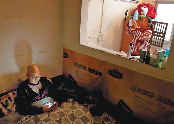 Shao Liangyu, 14, plays a game on a cellphone while his mother hangs up a surgical mask to dry in Wujianong, Hefei, Anhui province. Shao has acute myeloid leukemia. Situated next to the Anhui Provincial Children's Hospital, Wujianong is home to dozens of young cancer patients, most of whom come from rural areas and have to visit the hospital regularly for treatment. Gao Bo / for China Daily