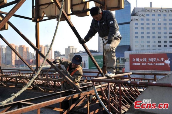 Workers remove signs atop a wholesale mall at Beijing Zoo Market in the citys Xicheng district on January 11, 2015. The mall named Tianhaocheng was the first one in the wholesale market area that had its signs removed. Most wholesalers have already moved out of the mall. With a business area of more than 300,000 square meters and 13,000 stalls, the Beijing Zoo Market represents the largest clothing wholesale distribution center in North China. The relocation project over the market is designed to improve downtown functions and relieve overcrowding and traffic jams. [Photo: chinanews.com/ Jin Shuo]