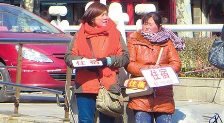 Two women with crudely made cardboard signs with the word zhu su (accommodation) wait near the citys Zhongshan Hospital for clients to come to them.  Wang Rongjiang