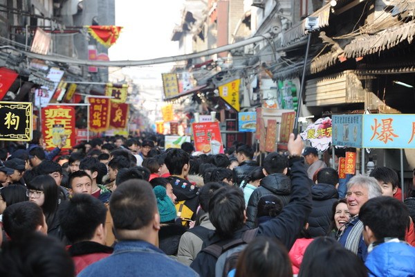 A young man takes a photo with a one-meter-long selfie stick attracting the attention of visitors the Furong Street, a tourist site in Jinan, capital of Shandong province. Photo by Chen Ning / For China Daily