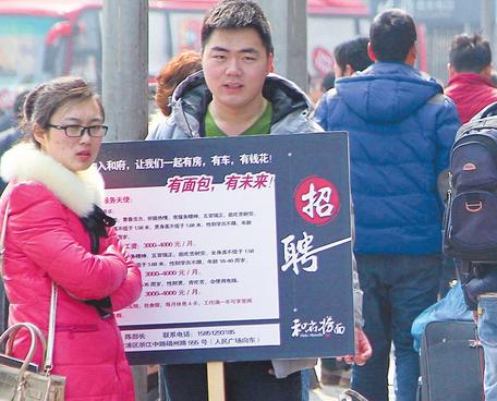A man stands outside the Shanghai Long-Distance Bus Station with a signboard offering jobs for migrant workers. Many local firms are struggling to recruit and retain skilled employees due to their increased wage demands. (Photo: Shanghai Daily/Dong Jun)