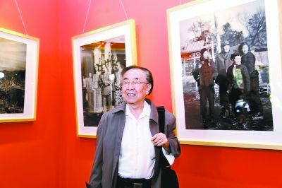 Lyu Houmin stands before his photos. (Photo/the Beijing Daily)