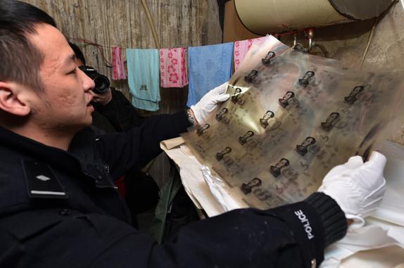 A policeman holds up a sheet used in making counterfeit money based on Peng Daxiang's artwork following a raid in Guangdong province on December 30. (Photo: Jing Guomin/China Daily)