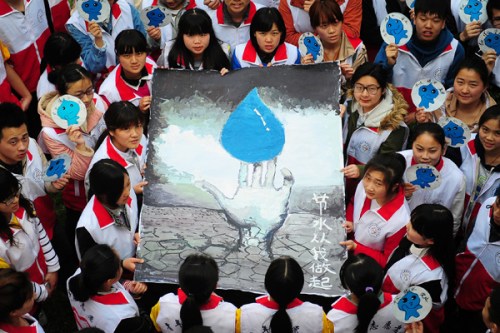 Volunteers at Fuyang Teachers College in Anhui province stand beside a painting with a water conservation theme intended to improve public awareness on Sunday. (Photo/China Daily) 