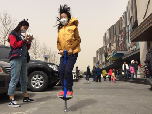 Residents wearing masks participate in outdoor activities on Lincui Road in Beijing on Saturday. The Beijing Meteorological Bureau issued a blue warning for a coming storm that was expected to increase dust levels. (Photo: Wang Jing/China Daily)  