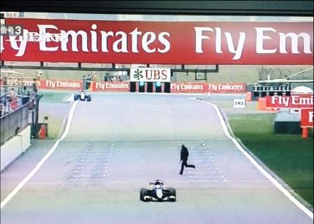 A television image shows a man, dressed indark clothes, narrowly avoiding speedingrace cars during a free practice yesterday atthe Shanghai International Circuit.