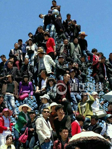 Dozens of tourists climb onto a climbing net on a wire frame to get a better view of a traditional performance celebrating a flower gala, April 14, 2015. (Photo/www.zjol.com.cn)