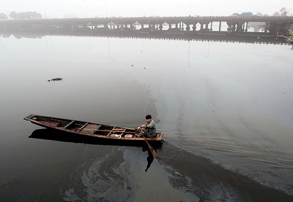 A man rows a boat through an oil slick on a lake in Shaoxing, Zhejiang province on March 16.Fuel leaking from ships severely contaminates the quality of the water in the lake. (Photo by Li Ruichang/China Daily)