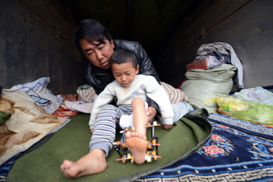 A Tibetan man helps his 7-year-old son, whose leg was injured in the quake. (Photo/Xinhua)