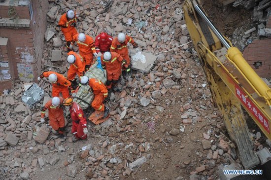 Rescuers carry a victim's body in Guiyang, capital of southwest China's Guizhou Province, May 21, 2015. Five bodies were found in the rubble of a collapsed building in central Guiyang Thursday. The accident happened on Wednesday, when the nine-story building with 114 residents living in it fell down. (Xinhua/Ou Dongqu)